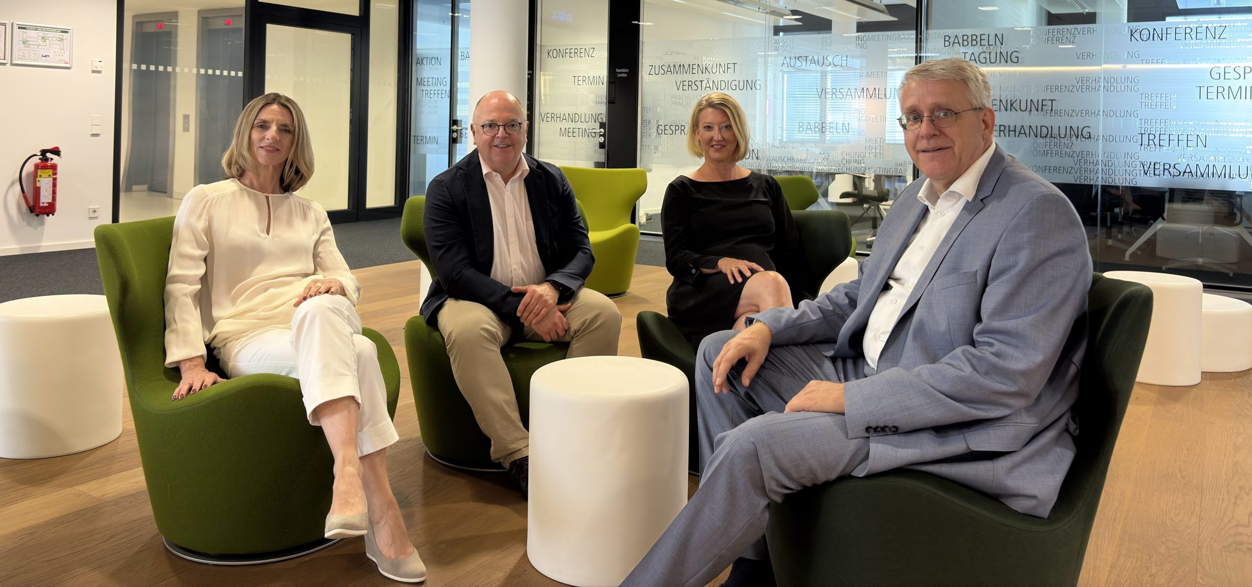 Content-Bild Gruppenfoto der vier Begründer des Performance-Fitness-Checks. Von links nach rechts: Sandra Oesterle, Bernd Schönwälder, Kerstin Kreutzer und Nikolaus Zumbusch. Alle vier Personen sitzen in einem Halbkreis in grünen Sesseln um einen kleinen weißen Tisch in einem modernen Bürogebäude und schauen lächelnd in die Kamera.